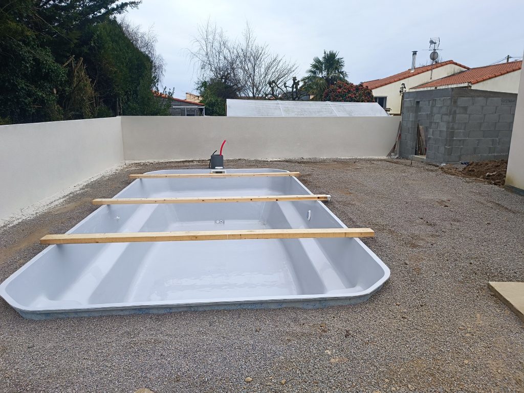 Coque de piscine posée sur son lit de gravier après terrassement