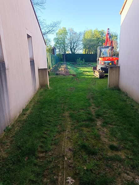 Pelle sur chenilles entrée dans un jardin par un passage étroit entre deux maisons