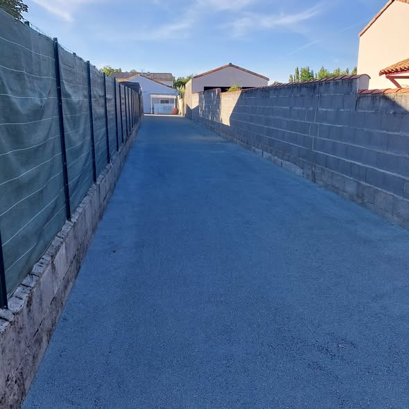Allée d'accès terminée entre mur et clôture, surface compactée