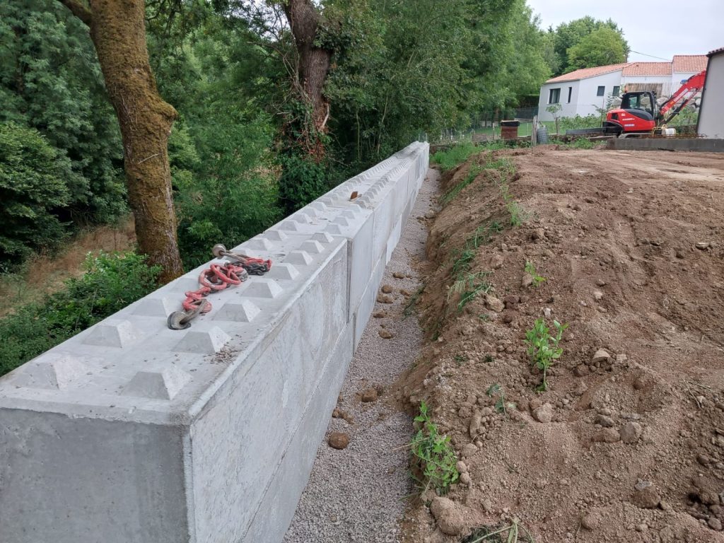 Mur de soutènement en blocs béton en cours de pose, pelle en fond