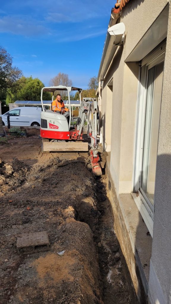 Mini-pelle creusant une tranchée de drainage le long d'une maison à Beaurepaire