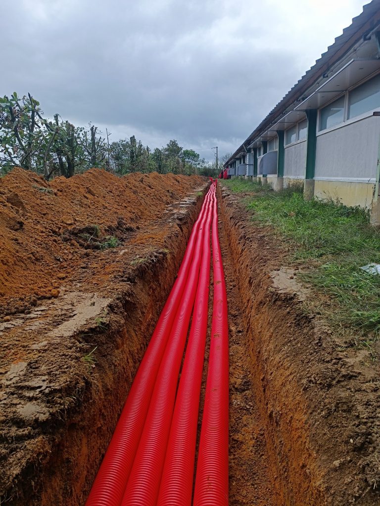 Pose de fourreaux électriques rouges au fond d'une tranchée